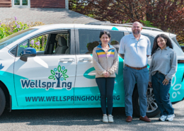Three staff from Wellspring's Homelessness Prevention program in front of the newly wrapped Wellspring hybrid passenger van, smiling during the ribbon-cutting celebration.